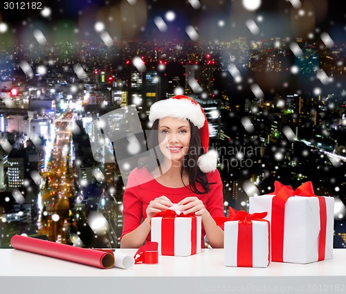 Image of smiling woman in santa helper hat packing gifts