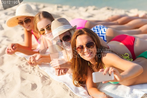 Image of group of smiling women with smartphone on beach