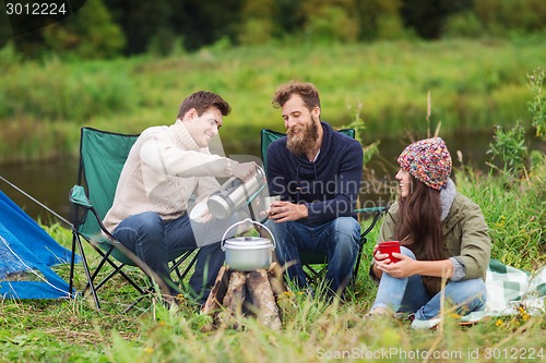 Image of group of smiling tourists cooking food in camping