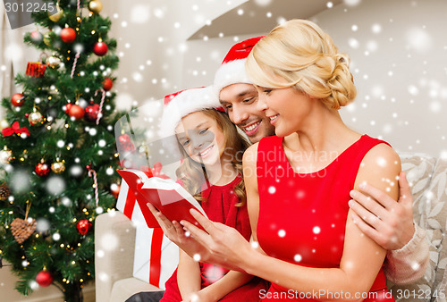 Image of smiling family in santa hats reading book at home