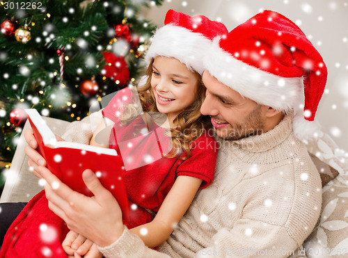 Image of smiling father and girl in santa hats reading book