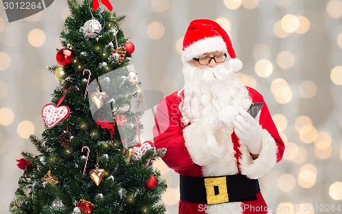 Image of santa claus with smartphone and christmas tree