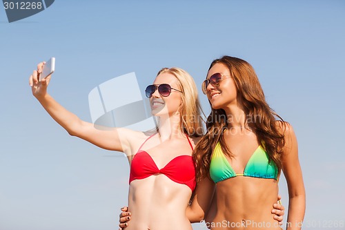 Image of two smiling women making selfie on beach