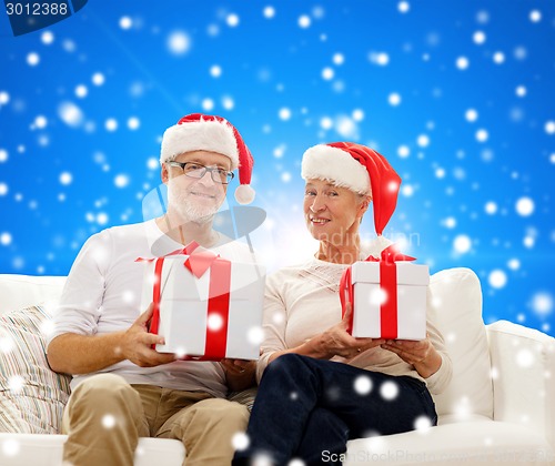 Image of happy senior couple in santa hats with gift boxes