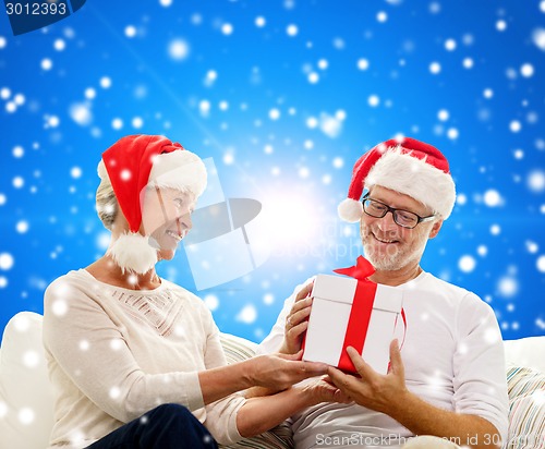 Image of happy senior couple in santa hats with gift box