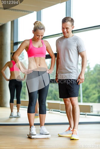 Image of smiling man and woman with scales in gym