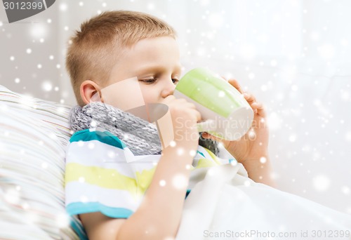 Image of ill boy with flu in bed drinking from cup at home