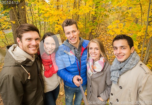 Image of smiling friends taking selfie in autumn park