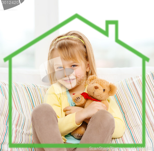 Image of smiling girl with teddy bear sitting on sofa