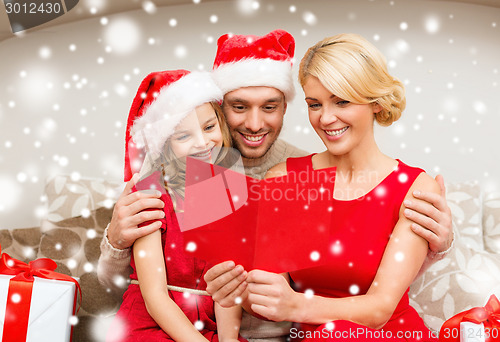 Image of smiling family in santa hats reading postcard