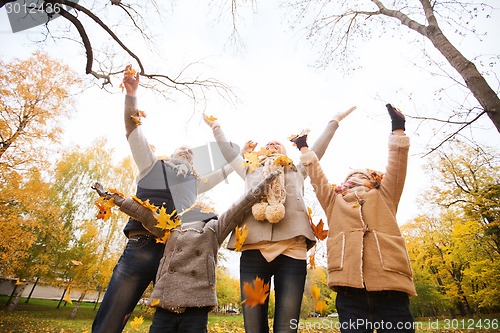 Image of happy family playing with autumn leaves in park