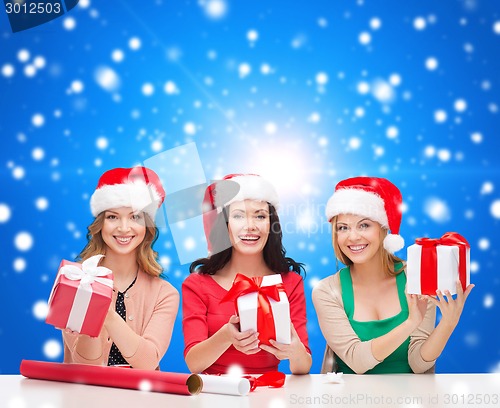 Image of smiling women in santa helper hats packing gifts