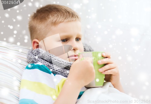 Image of ill boy with flu in bed drinking from cup at home