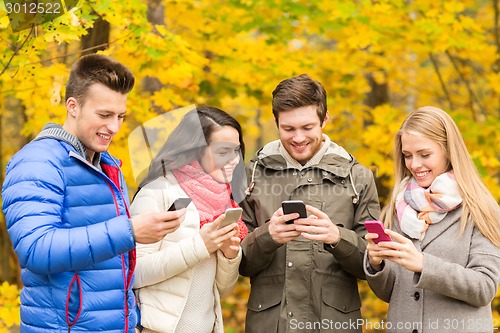 Image of smiling friends with smartphones in city park