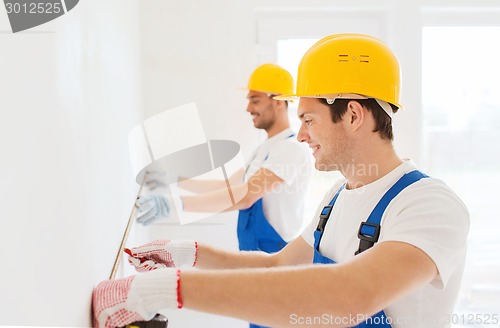 Image of smiling builders with measuring tape indoors