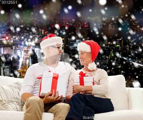 Image of happy senior couple in santa hats with gift boxes