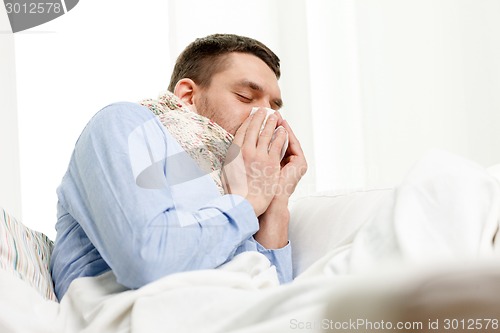 Image of ill man in scarf blowing nose at home