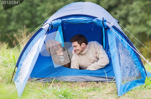 Image of smiling couple of tourists looking out from tent