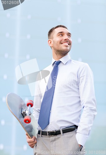 Image of young smiling businessman with skateboard outdoors