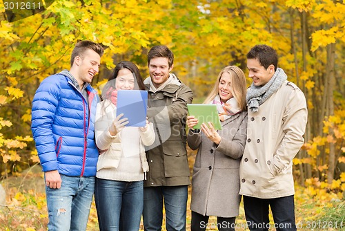Image of group of smiling friends with tablets in park