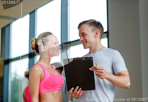 Image of smiling young woman with personal trainer in gym