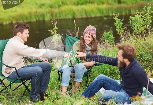 Image of group of smiling tourists drinking beer in camping