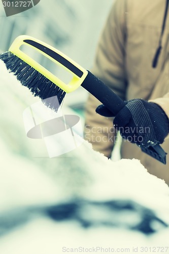 Image of man cleaning snow from car windshield with brush