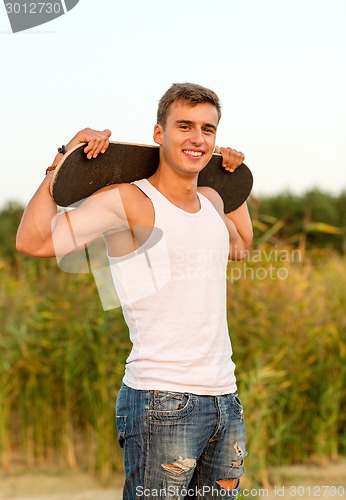 Image of smiling teenage boy with skateboard outdoors