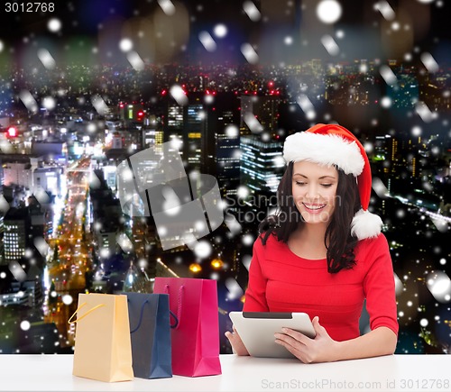 Image of smiling woman in santa hat with bags and tablet pc