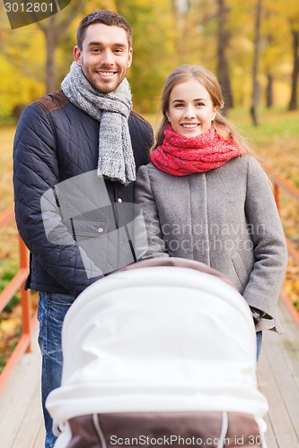 Image of smiling couple with baby pram in autumn park