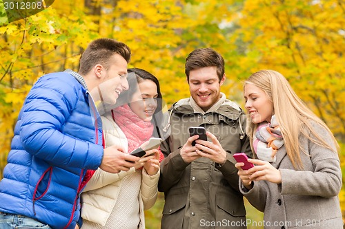 Image of smiling friends with smartphones in city park