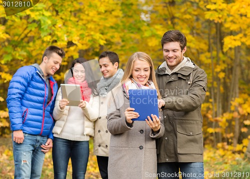 Image of group of smiling friends with tablets in park
