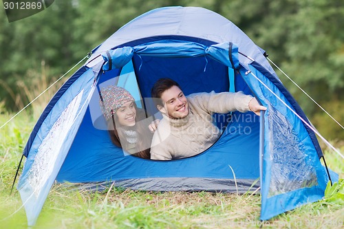 Image of smiling couple of tourists looking out from tent