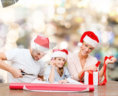 Image of happy family in santa helper hats packing gift