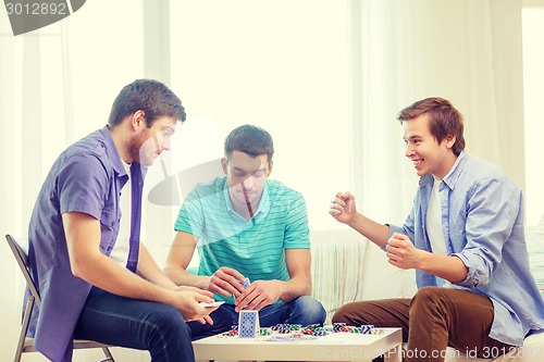 Image of happy three male friends playing poker at home