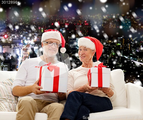 Image of happy senior couple in santa hats with gift boxes