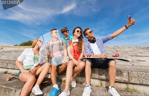 Image of group of smiling friends with smartphone outdoors