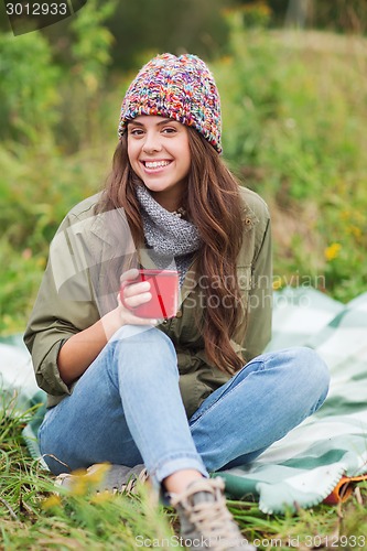 Image of smiling young woman with cup sitting in camping