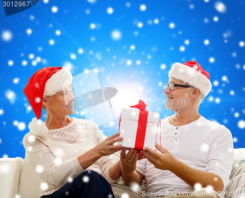 Image of happy senior couple in santa hats with gift box