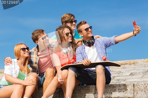 Image of group of smiling friends with smartphone outdoors