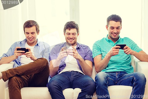 Image of smiling friends with smartphones at home