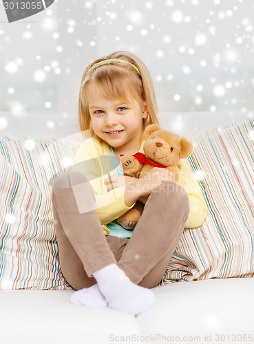 Image of smiling girl with teddy bear sitting on sofa