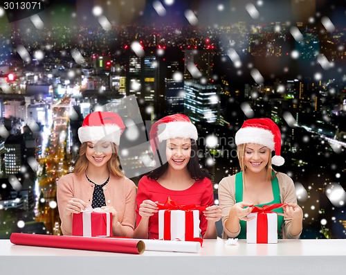 Image of smiling women in santa helper hats packing gifts