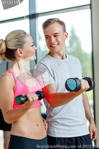 Image of smiling young woman with personal trainer in gym