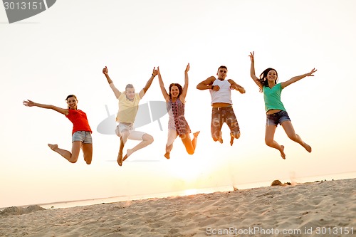 Image of smiling friends dancing and jumping on beach