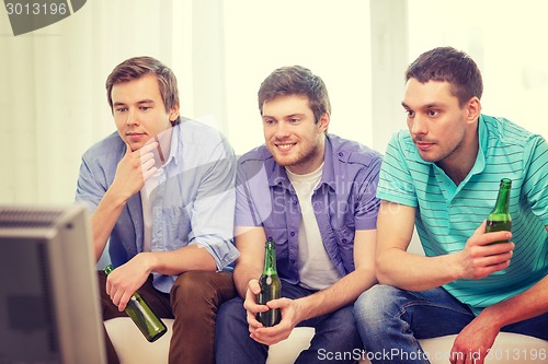 Image of happy male friends with beer watching tv at home