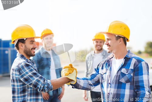 Image of group of smiling builders shaking hands outdoors