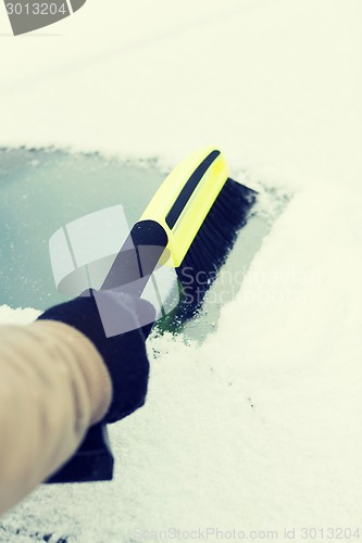 Image of man cleaning snow from car windshield with brush