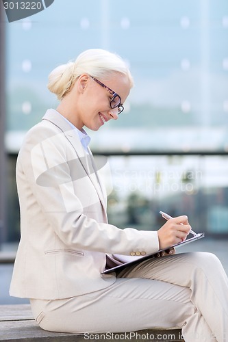 Image of young smiling businesswoman with notepad outdoors