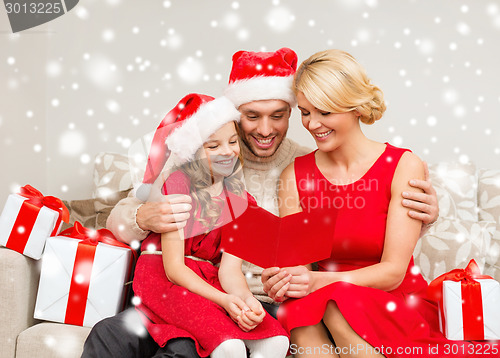 Image of smiling family in santa hats reading postcard